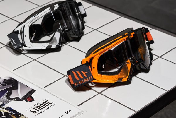 Мотоочки белые и оранжевые на белом столе в магазине мотоэкипировки. Торговое оборудование из белой плитки.