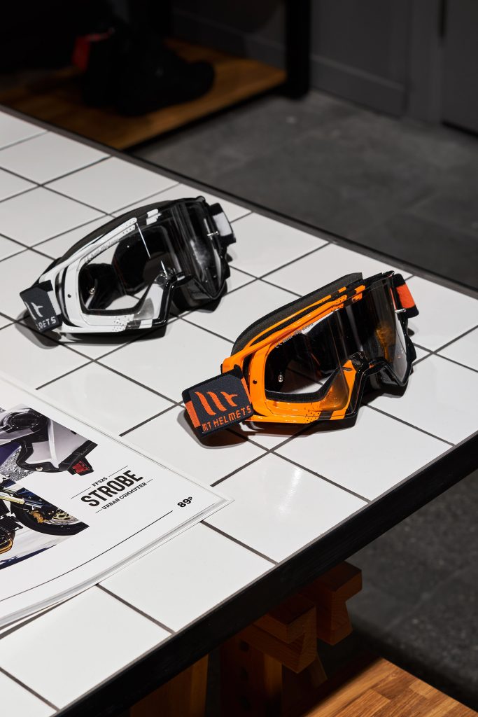 Мотоочки белые и оранжевые на белом столе в магазине мотоэкипировки. Торговое оборудование из белой плитки.