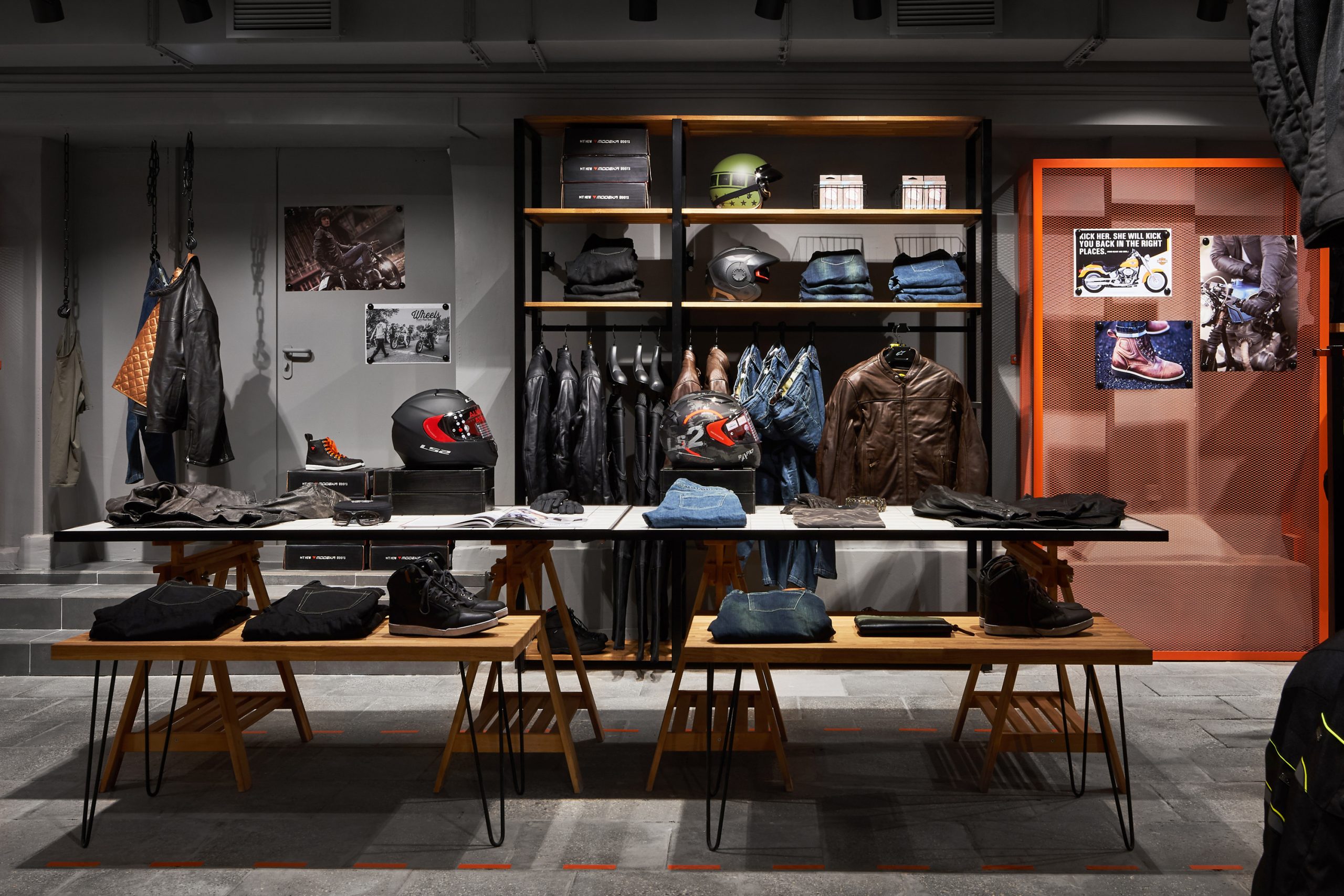 Торговый зал мотосалона с мотошлемами и защитной экипировкой на торговом оборудовании и столах из белок плитки.