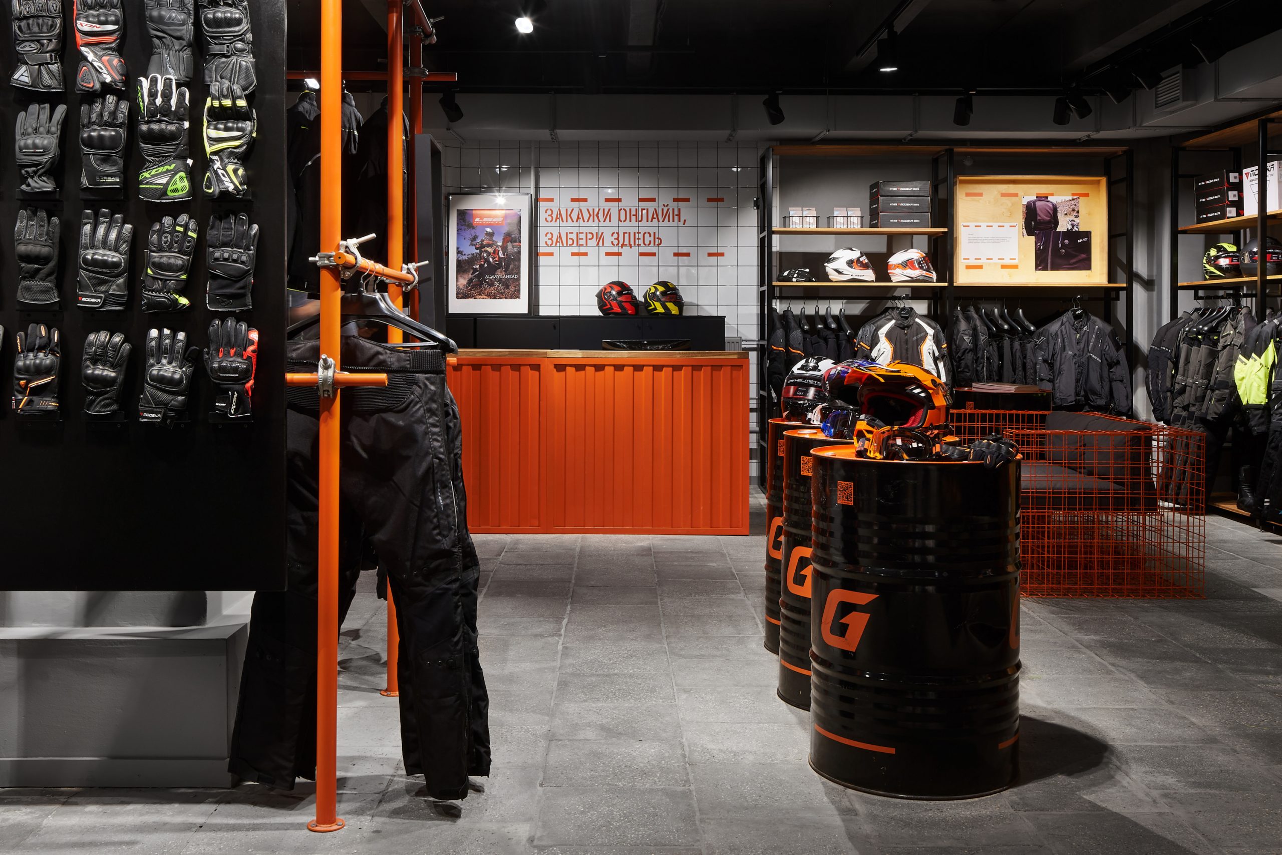 Интерьер мотосалона с мотоэкипировкой и оранжевой кассой из профлиста и торговым оборудованием для шлемов.