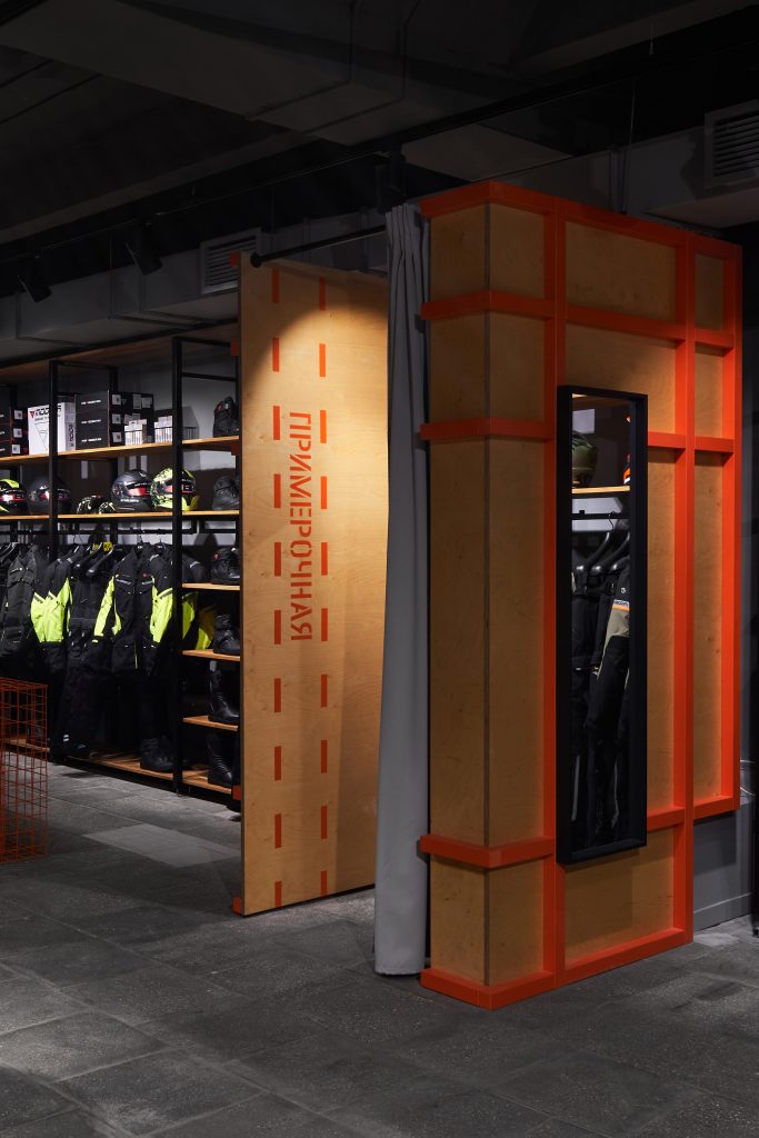 Интерьер мотосалона с оранжевой примерочной из фанеры. Графический дизайн.