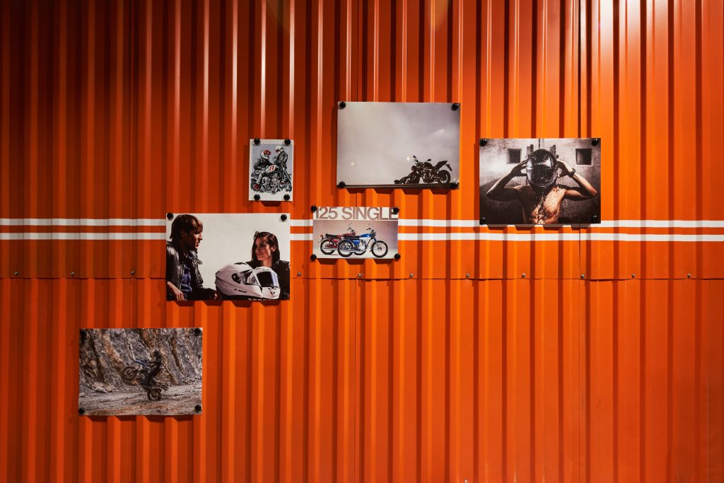 Оранжевая стена из профлиста в дизайне мотосалона с мотопостерами и белыми полосами в мотосалоне как разметка на дороге.