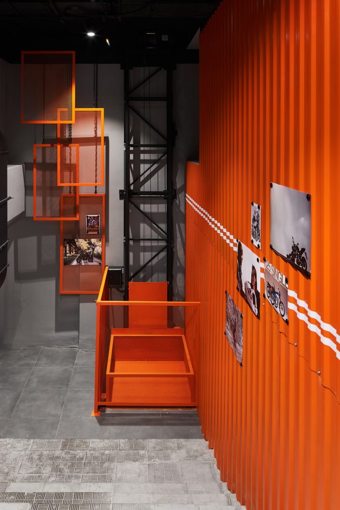 Входная зона в магазин Оранжевая стена из профлиста RAL 3000 и мотопостеры на магнитах и белые полосы стилизующие дорожную разметку.