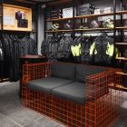 Зона одыха в мотосалоне. Диван из оранжевой металлической сетки и мягкие подушки. Торговое оборудование и мотоэкипировка.